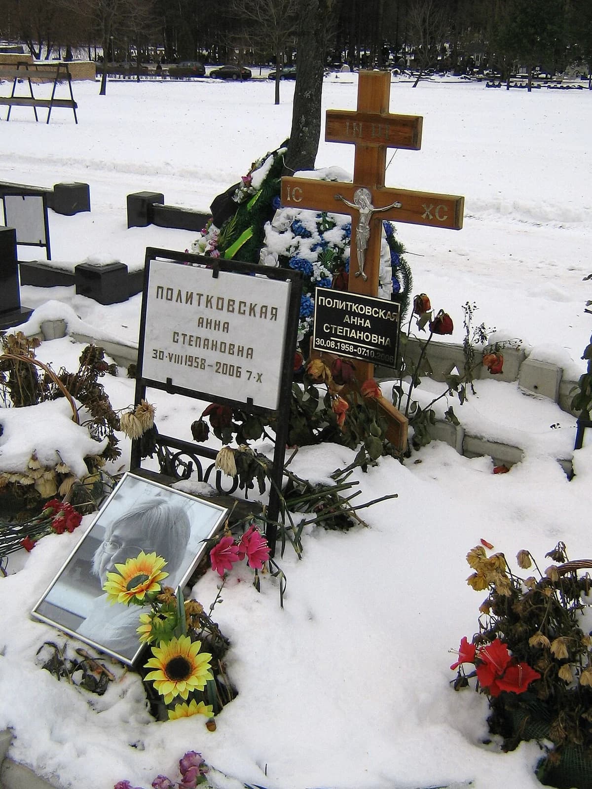 Anna Politkovskaya's grave covered in snow with crosses, plaques, flowers, and a portrait.