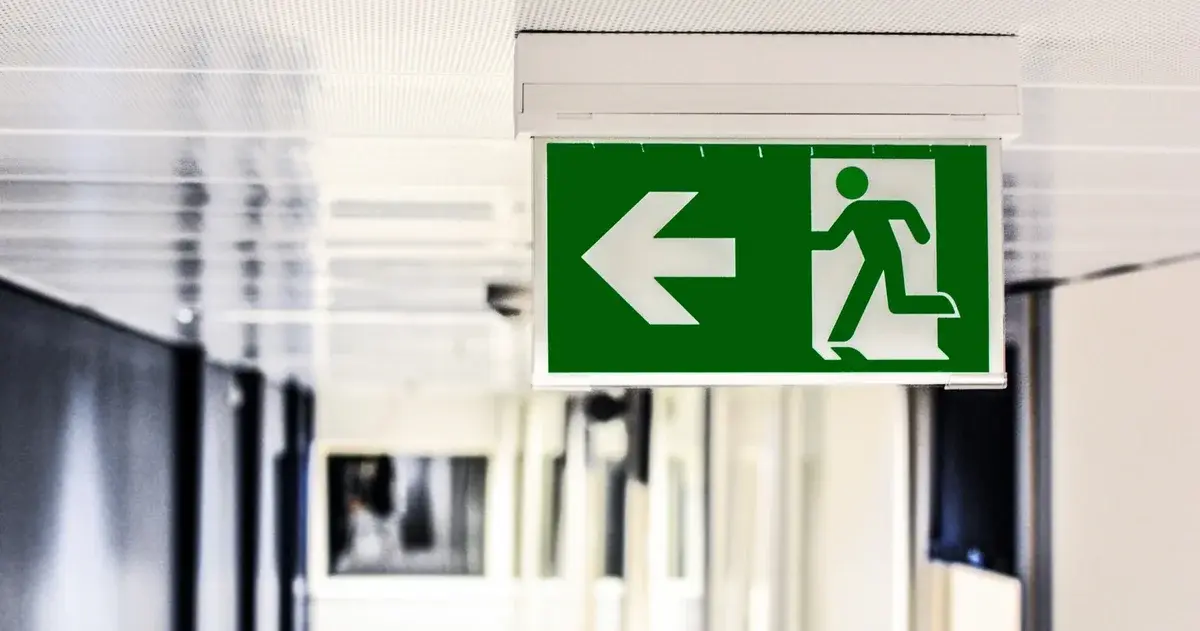 Green emergency exit sign with left arrow hanging in a hallway