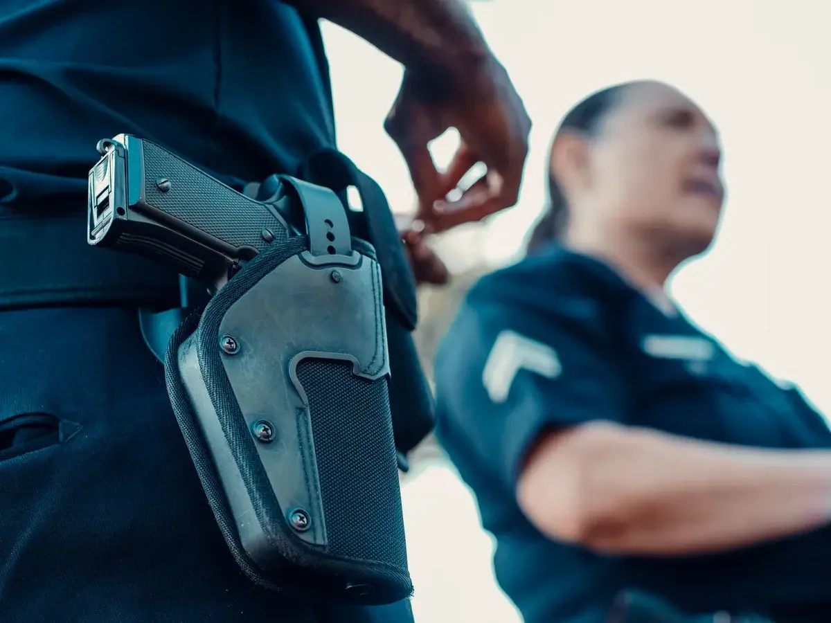 Close-up of a police officer's holstered pistol with another officer blurred behind.