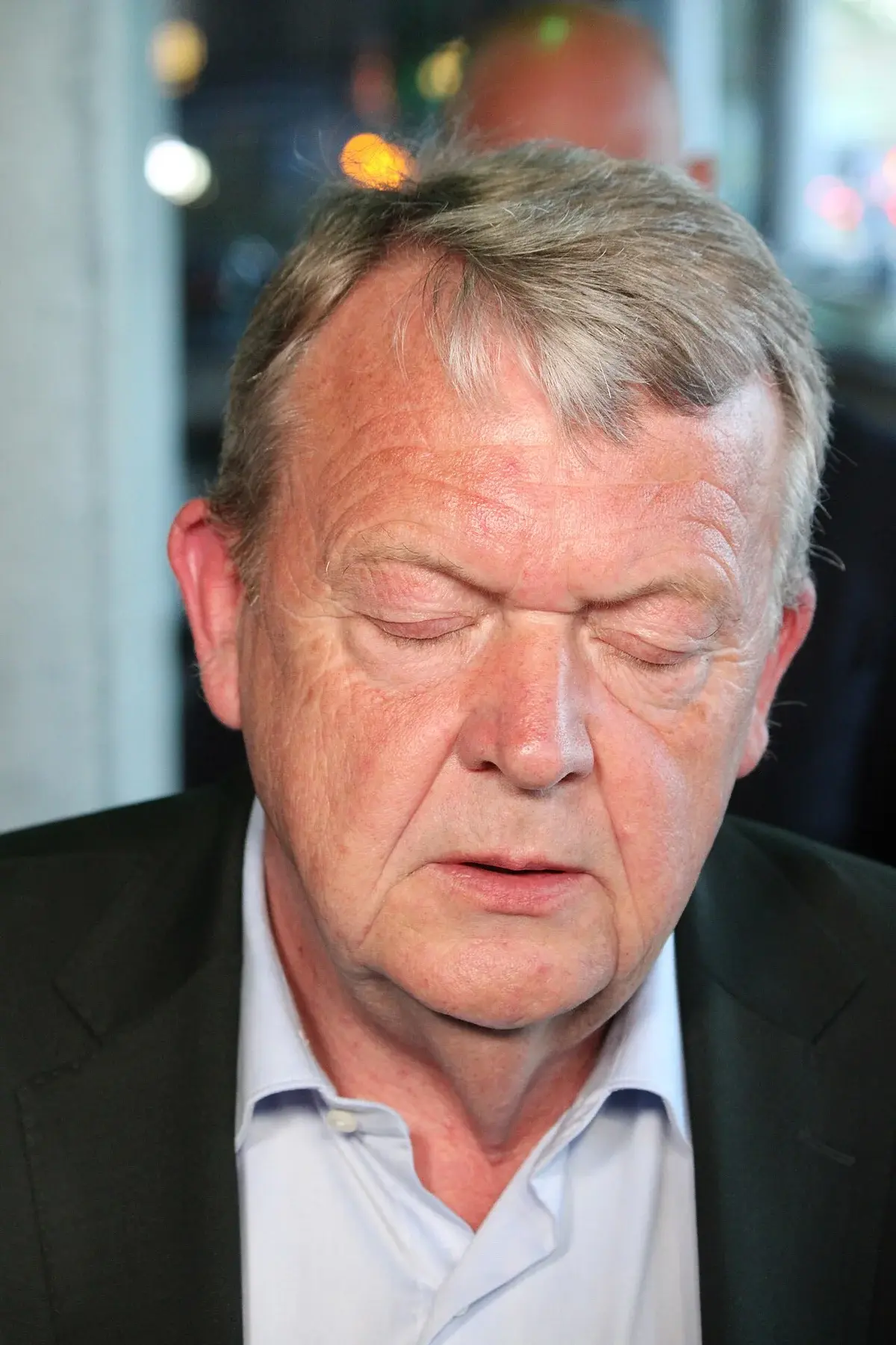Close-up of Lars Løkke Rasmussen speaking to reporters indoors.
