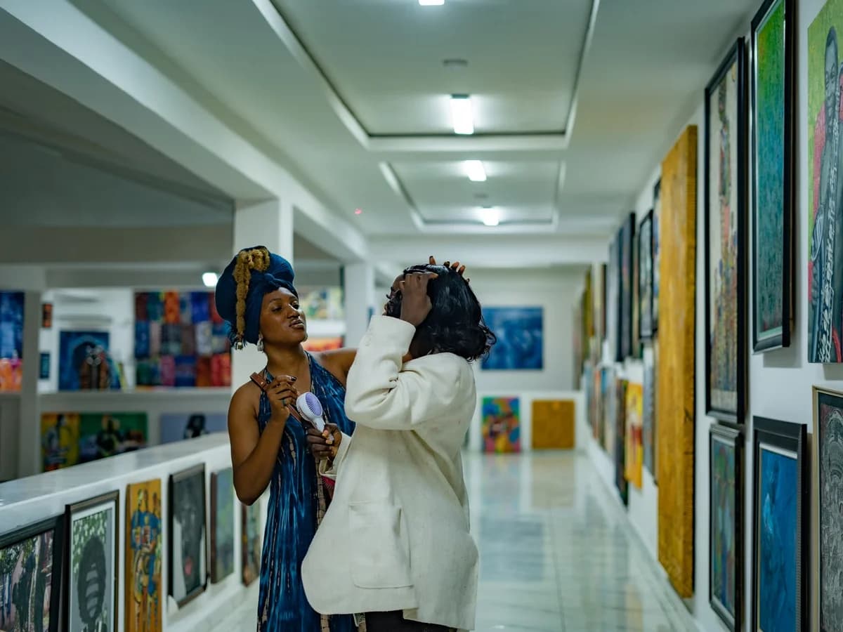 Two adults standing and talking in an art gallery surrounded by colorful paintings.