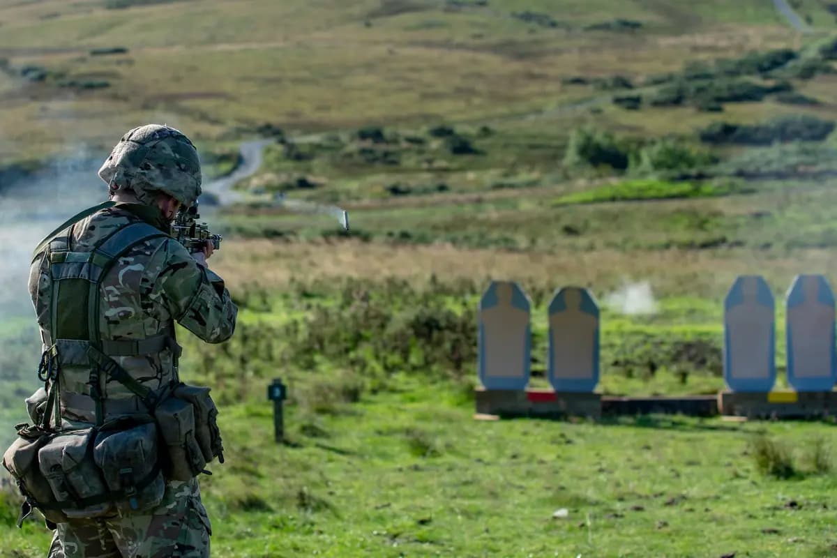 A soldier in military gear engages in shooting practice on an outdoor range.
