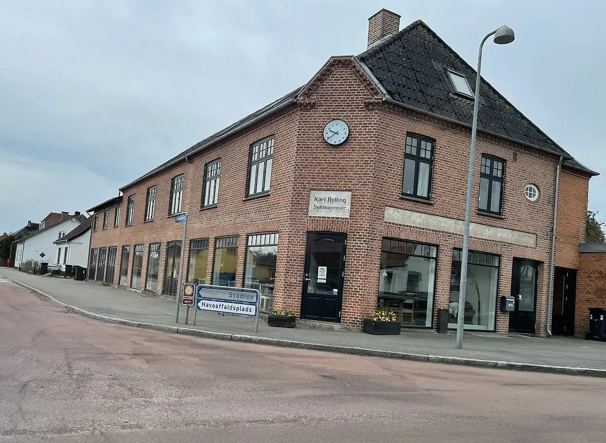 Brick building on a street corner with a clock on the facade and road signs in front.