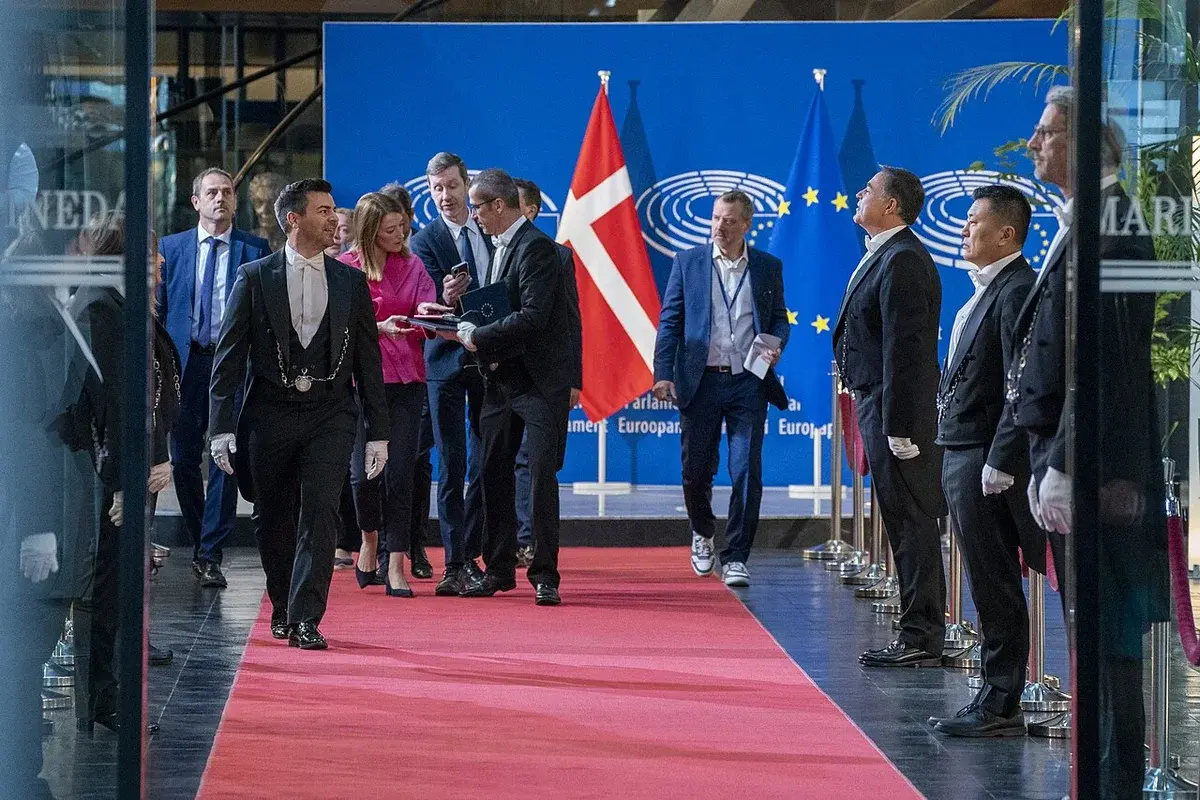Officials and security staff on a red carpet at a European Parliament venue with EU and Danish flags.