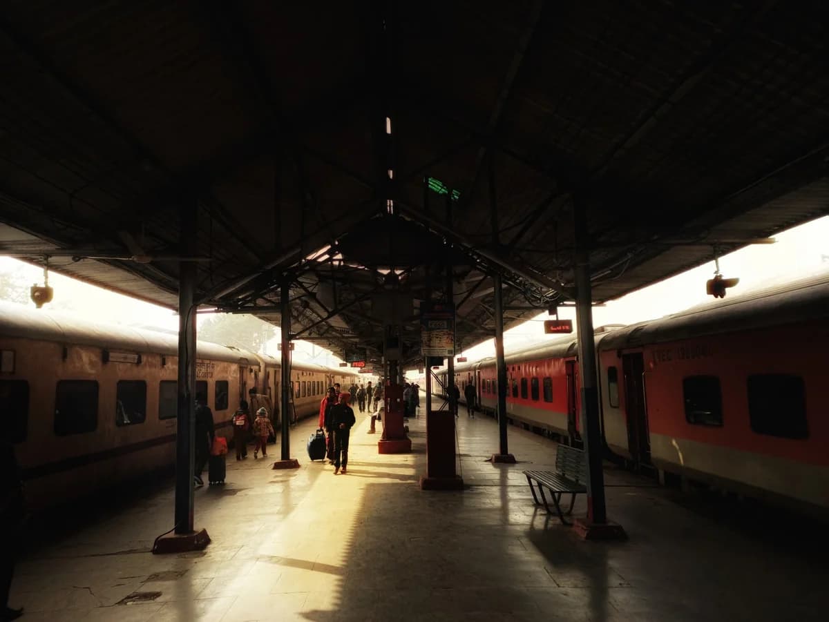 People with luggage on a railway platform between parked trains in Lucknow, India.