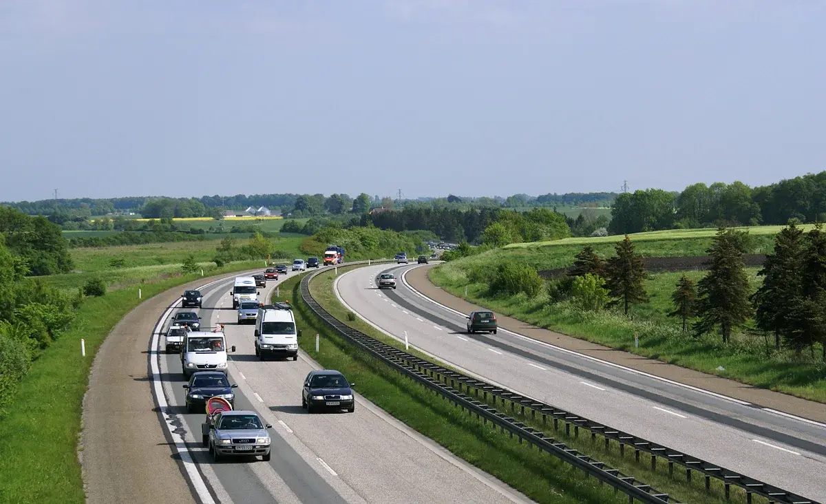 Cars and vans driving on a highway through green countryside.