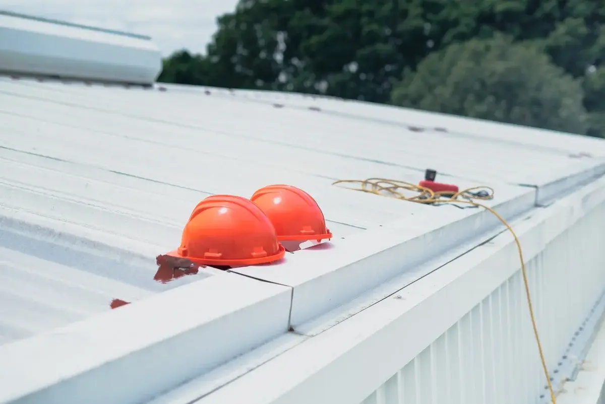 Two red safety helmets on a metal roof with rope and tools nearby.