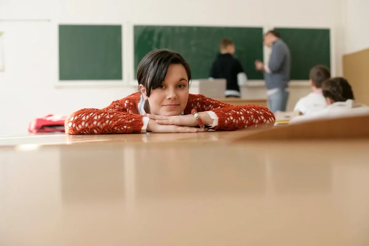 A student resting her head on a desk in a classroom.