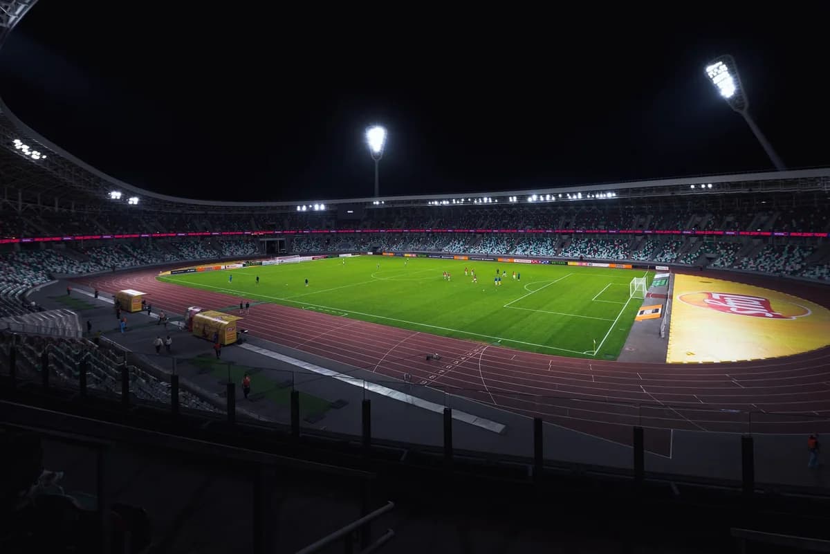 A night view of a football stadium with players on the field and empty stands.