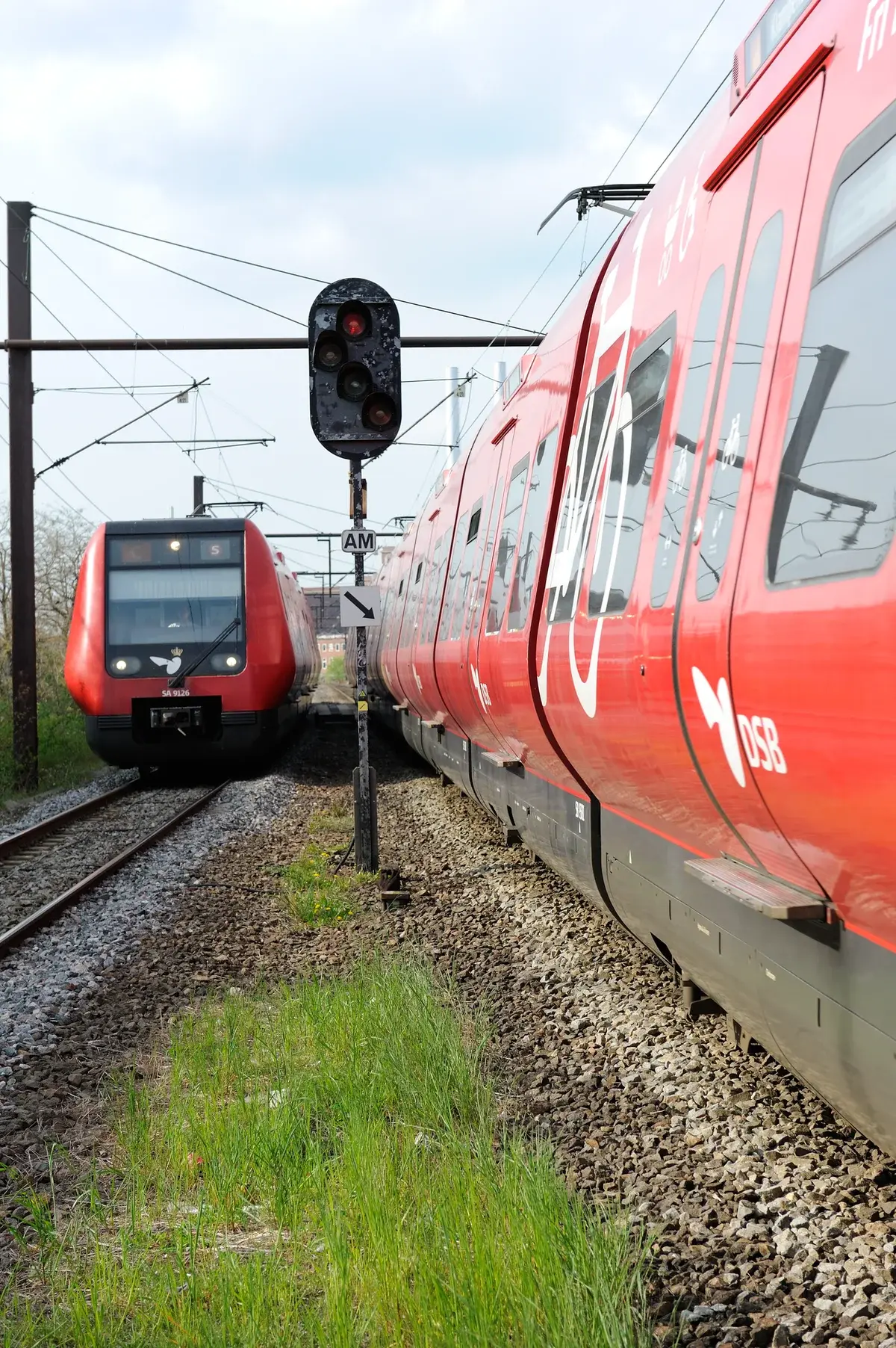 Two red DSB S-trains pass each other on tracks in Copenhagen.