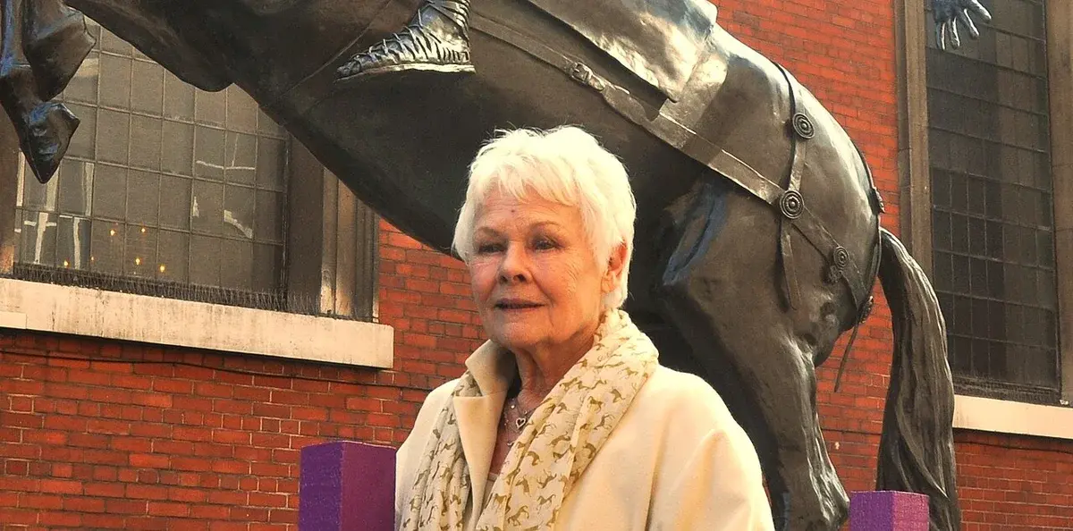 Judi Dench standing in front of a large statue during a public unveiling ceremony.