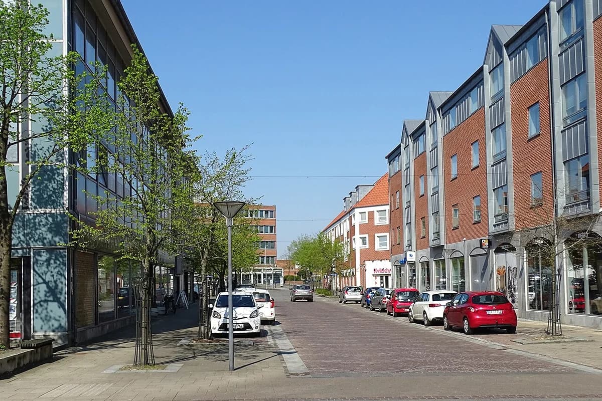 A quiet street in Vejen with parked cars and modern buildings on both sides.