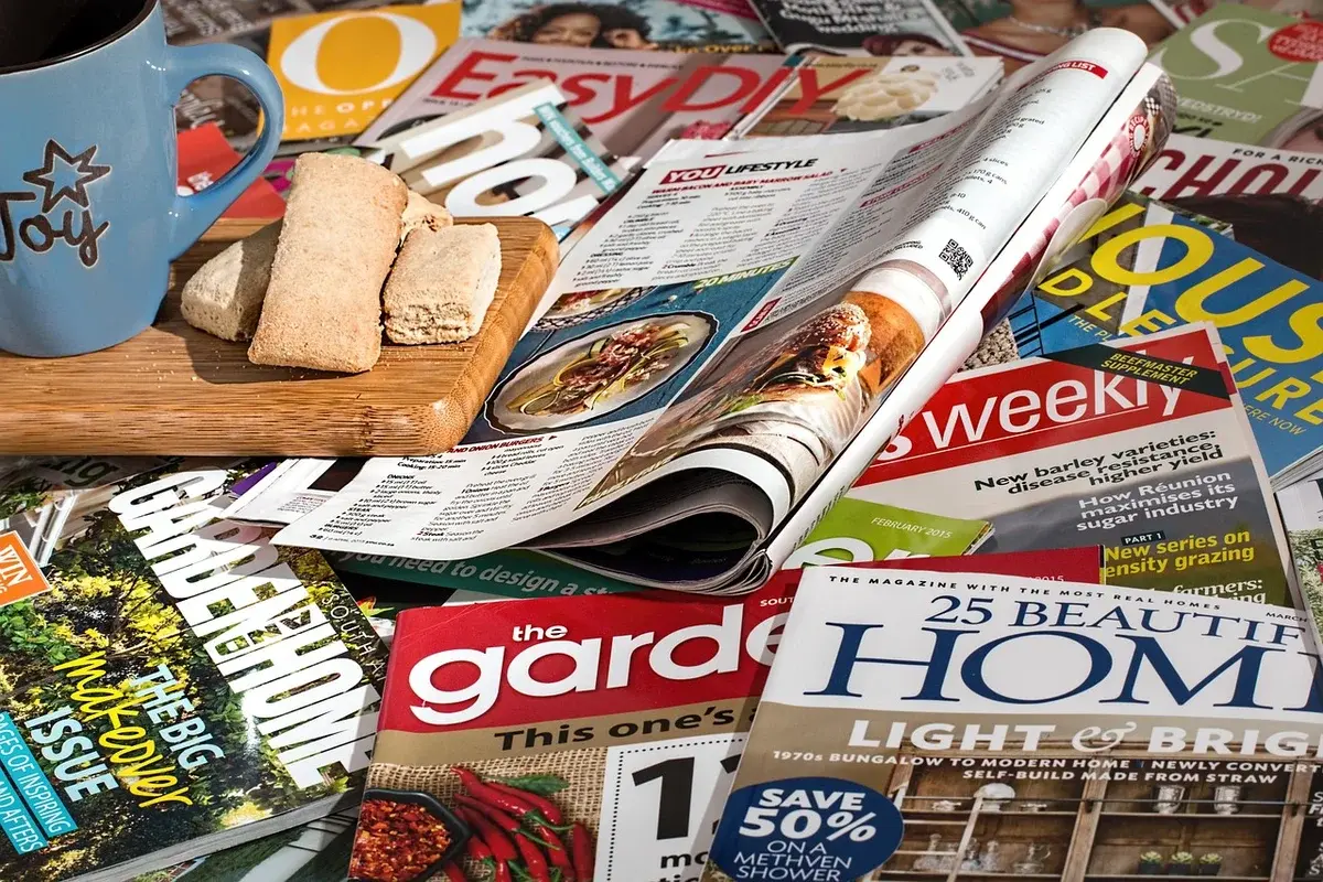 A spread of magazines with a blue mug and a small tray of bread or crackers.