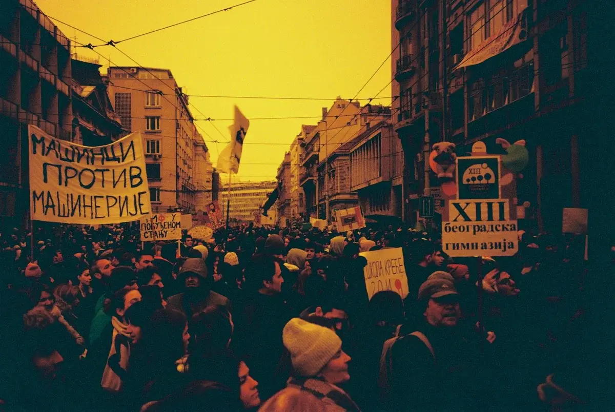 A crowded protest march fills a city street beneath tram wires.