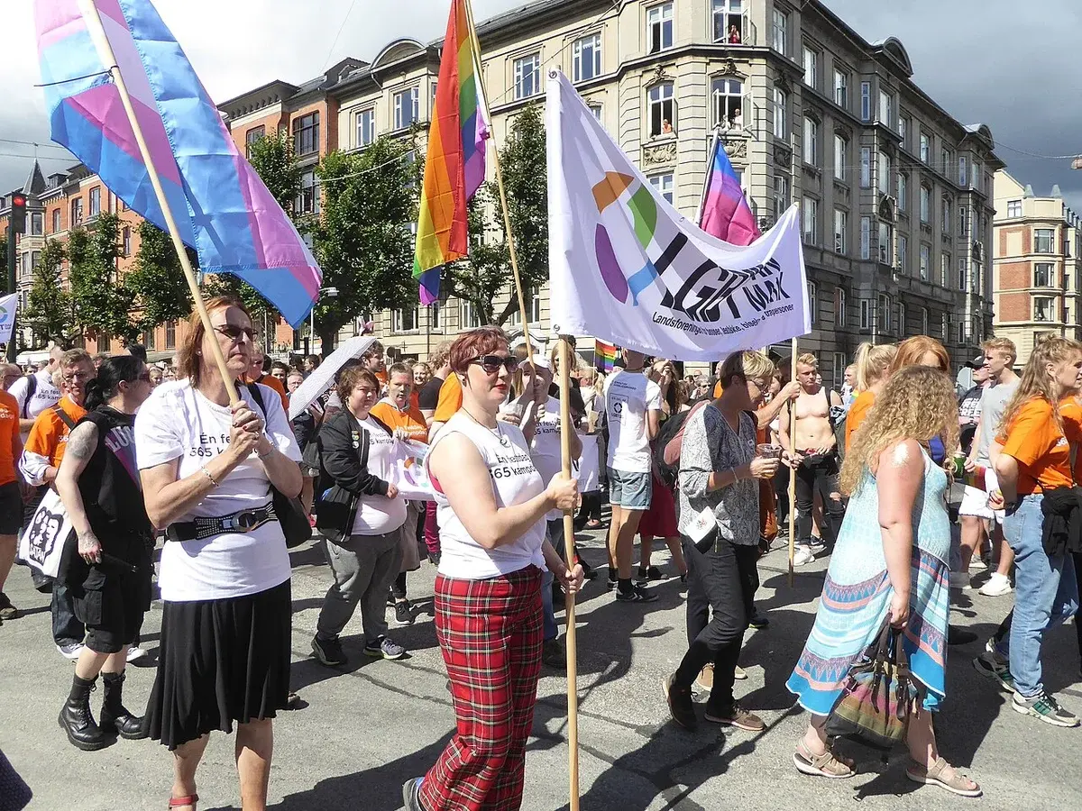 People marching in a Copenhagen Pride parade carrying rainbow flags.