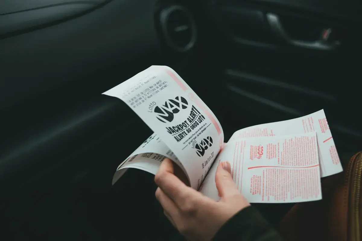 hands holding Lotto Max lottery tickets in a car