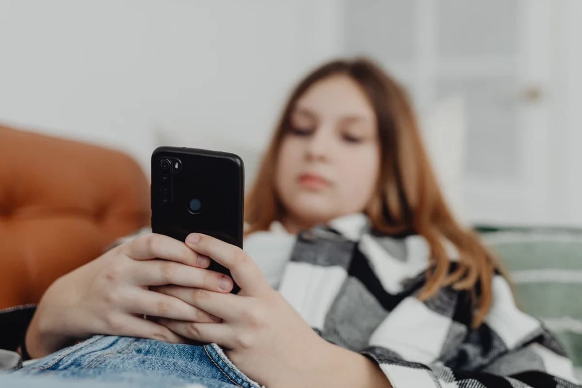 Teenage girl relaxing on a sofa while using a smartphone.