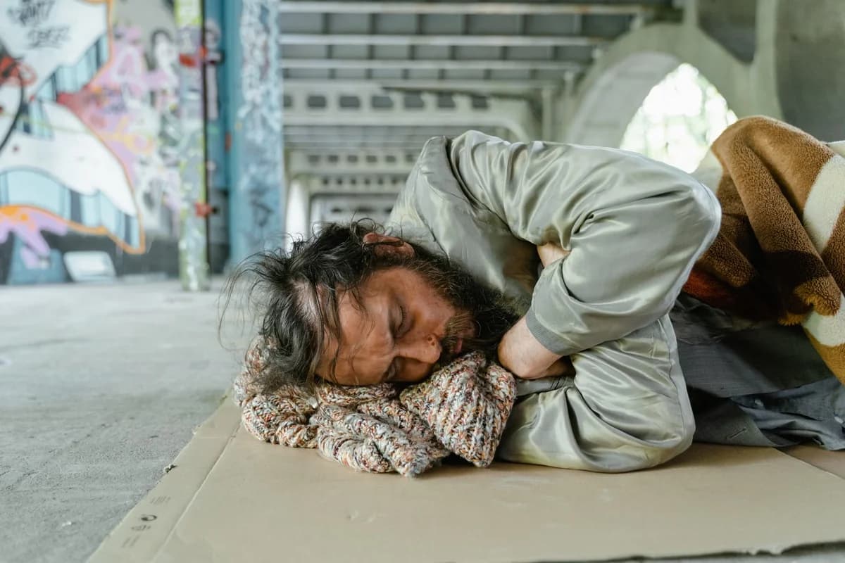 Homeless man sleeping on cardboard under a graffiti-covered bridge
