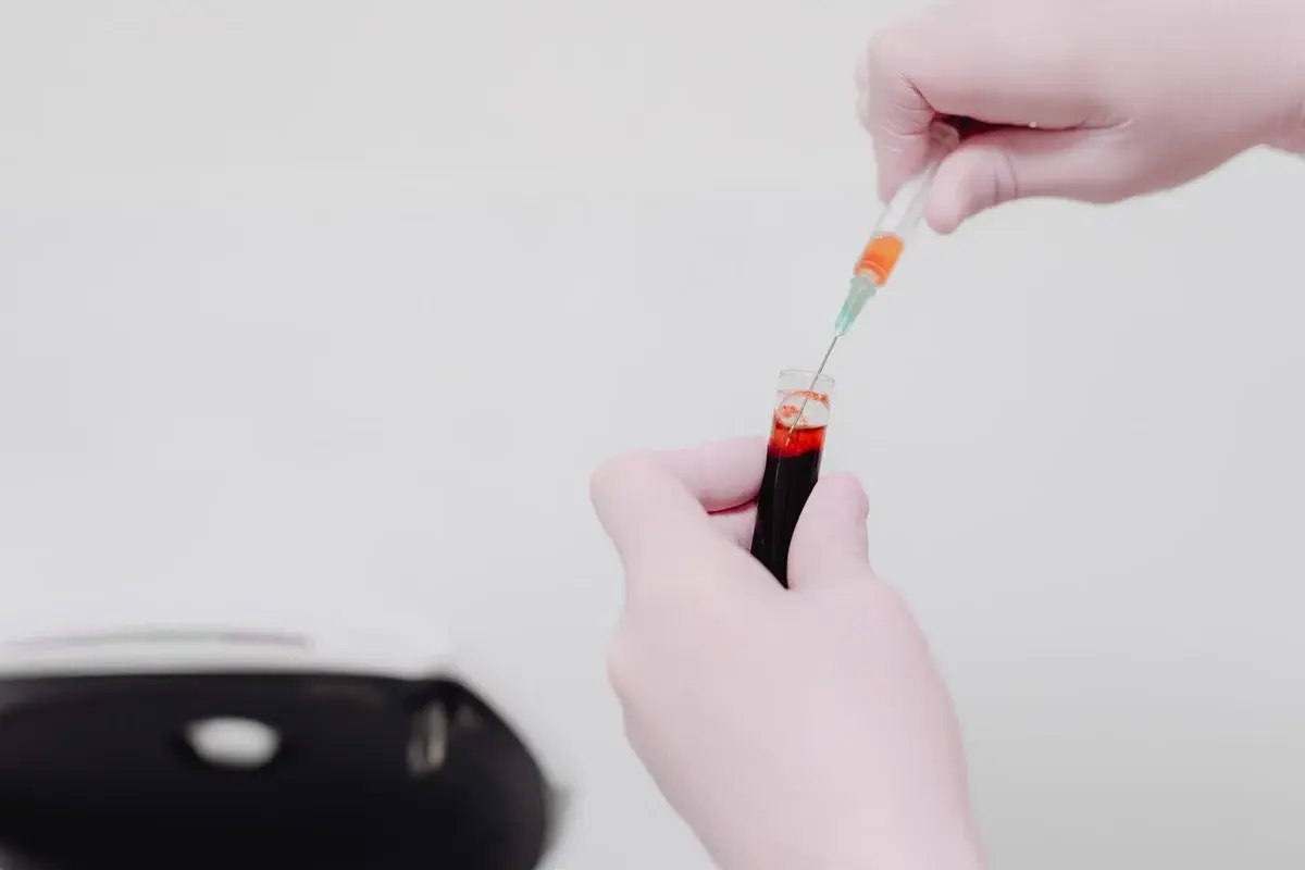 Gloved hands using a syringe to transfer blood from a test tube.