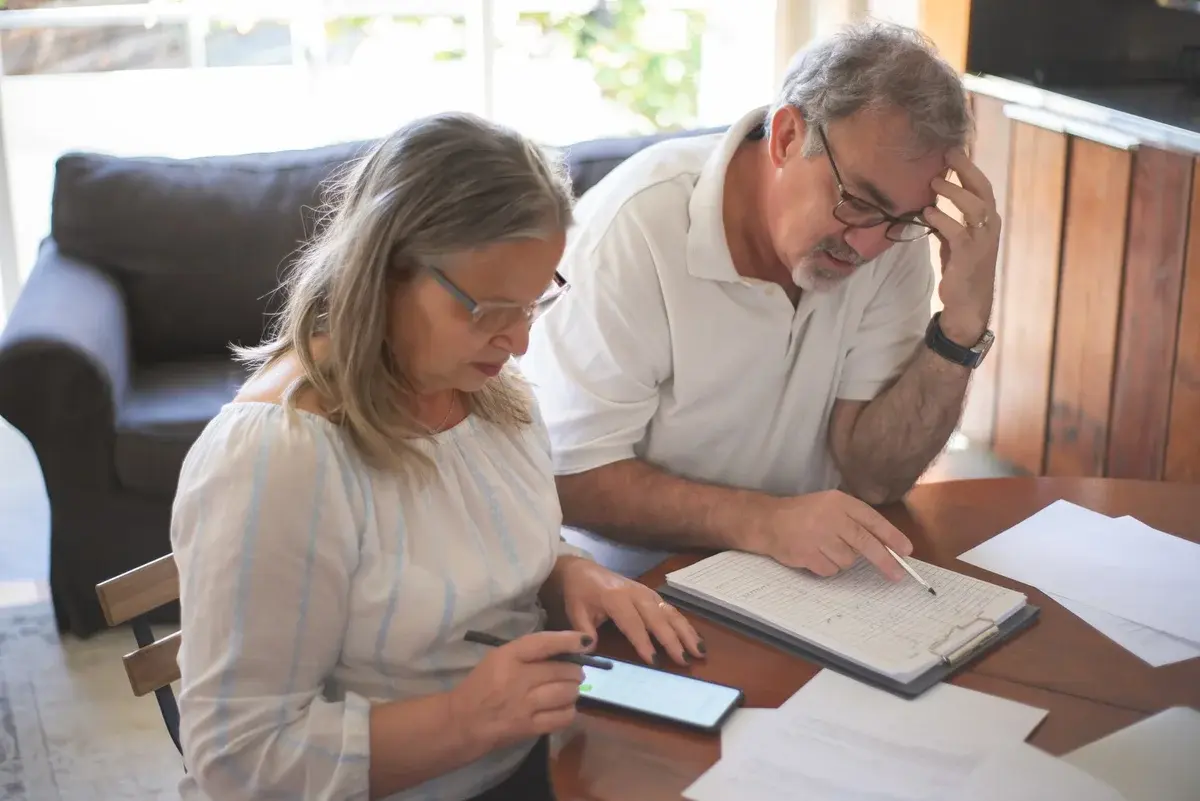 An older couple reviews bills and paperwork at a table in their home.