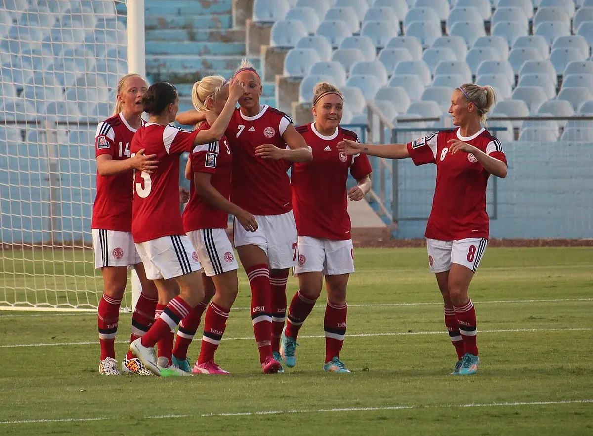 Danish women soccer players celebrating a goal near the net.