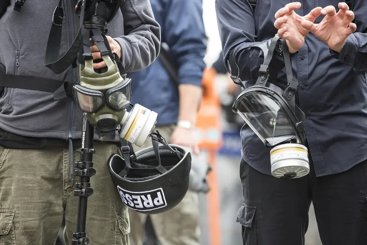 Two press workers wearing gas masks in a tense protest scene.