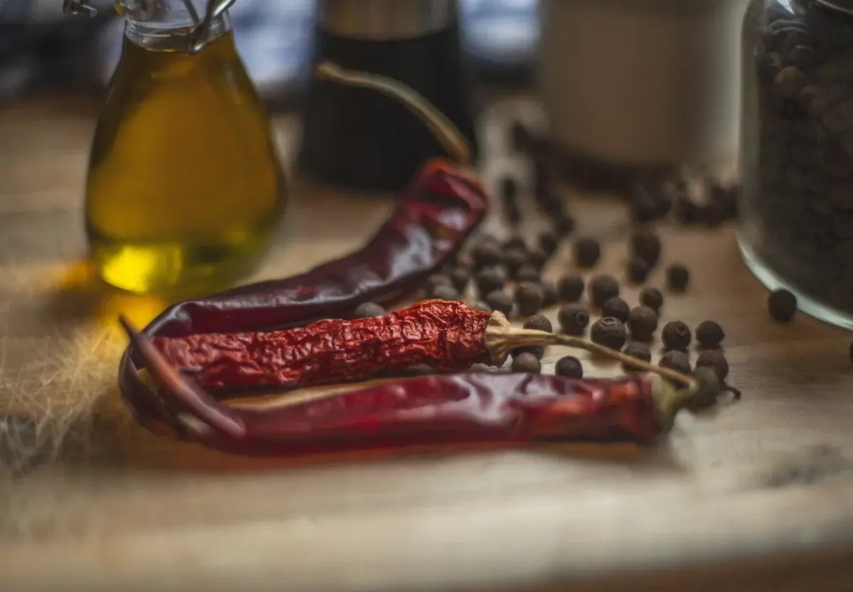 Dried chilies, peppercorns, and olive oil on a wooden table.