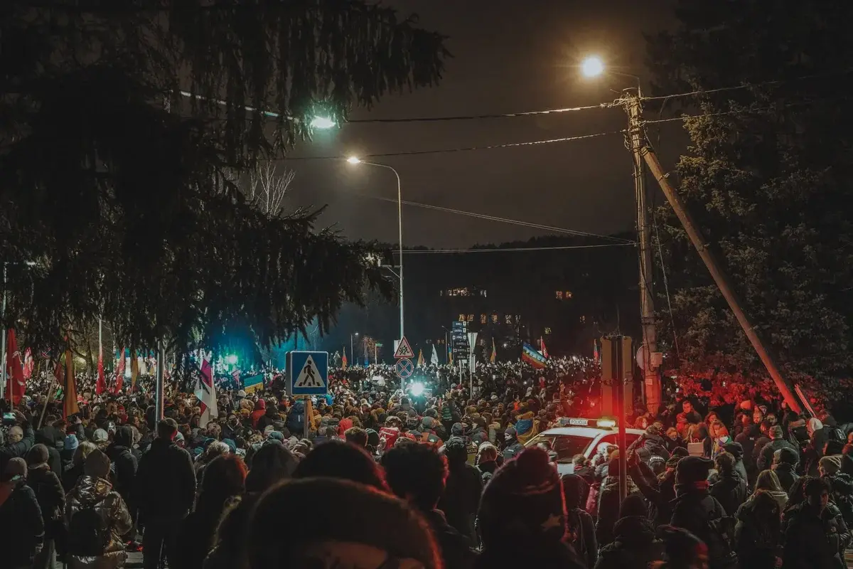 Crowded nighttime street protest with flags and police lights