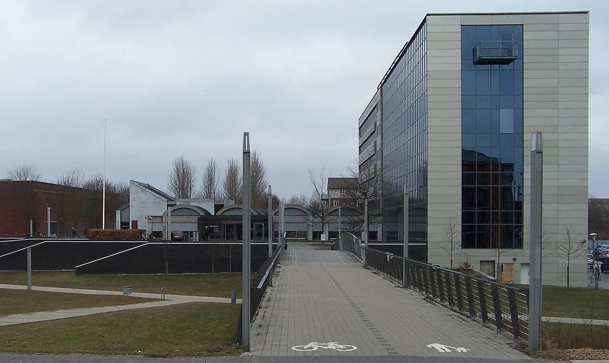 Modern town hall building with a glass facade and a pedestrian and bicycle path leading to the entrance under a cloudy sky.