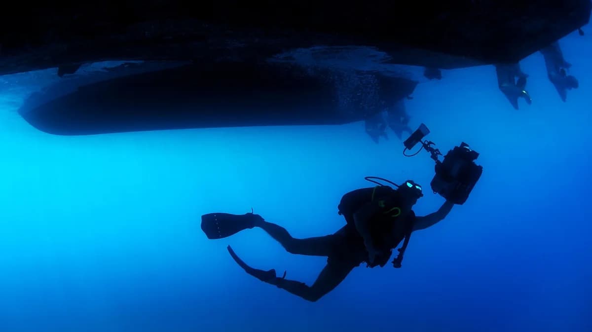 Scuba diver underwater holding a camera near a boat propeller