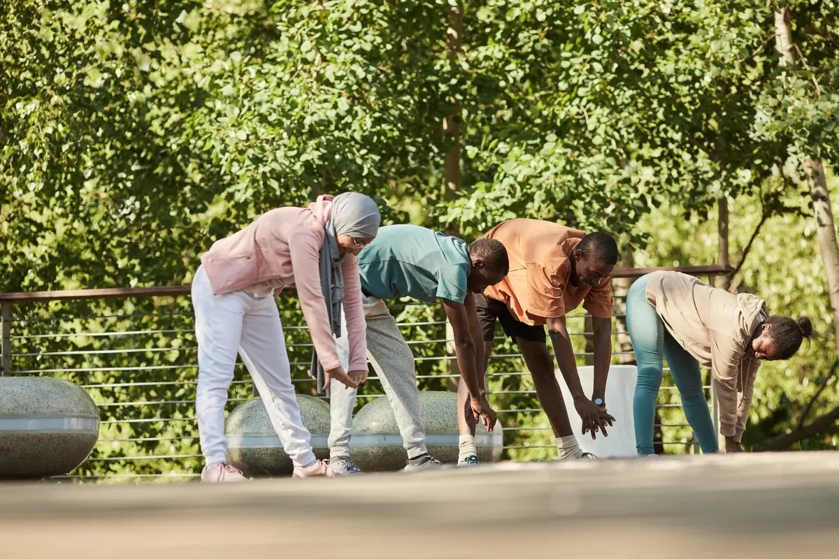 Four adults stretching outdoors in a park