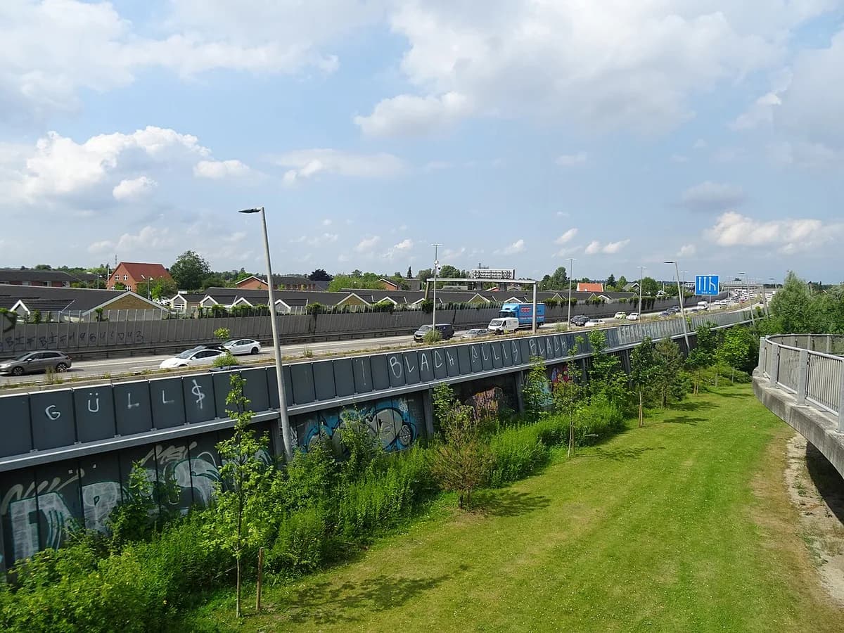 Traffic on a Danish motorway beside graffiti-covered walls and houses.