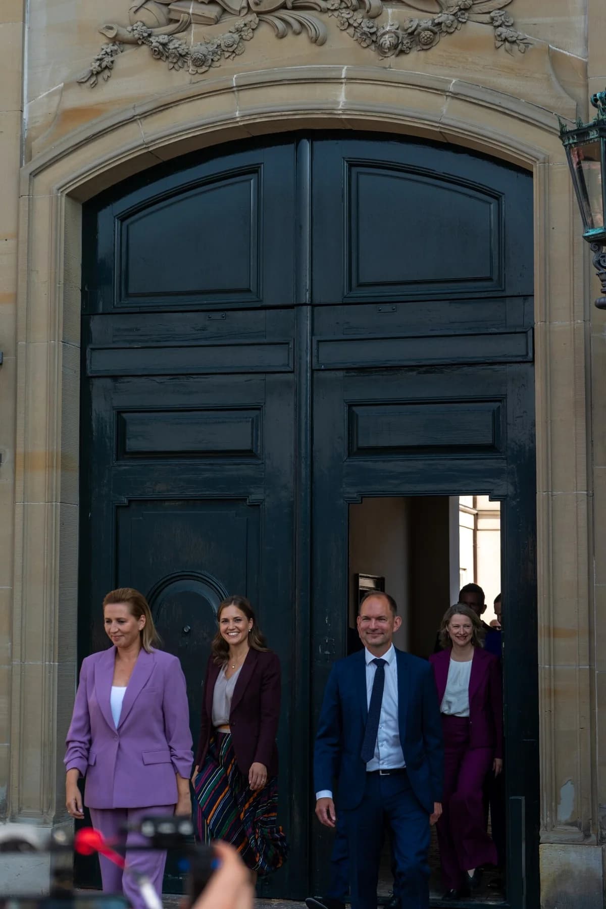 Several Danish politicians walk out of a large ornate doorway at Amalienborg.