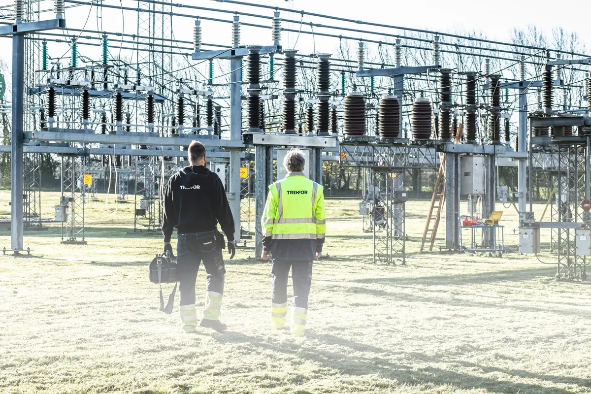 Two workers inspect an outdoor electrical substation.