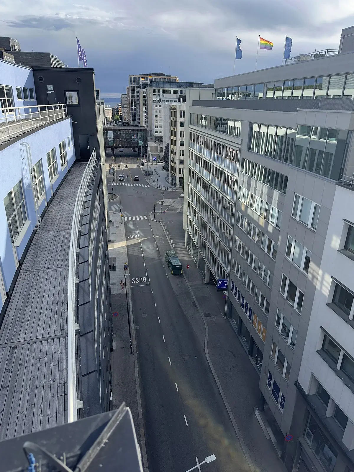 High-angle rooftop view over a street in central Oslo, with modern buildings and flags on the rooftops.