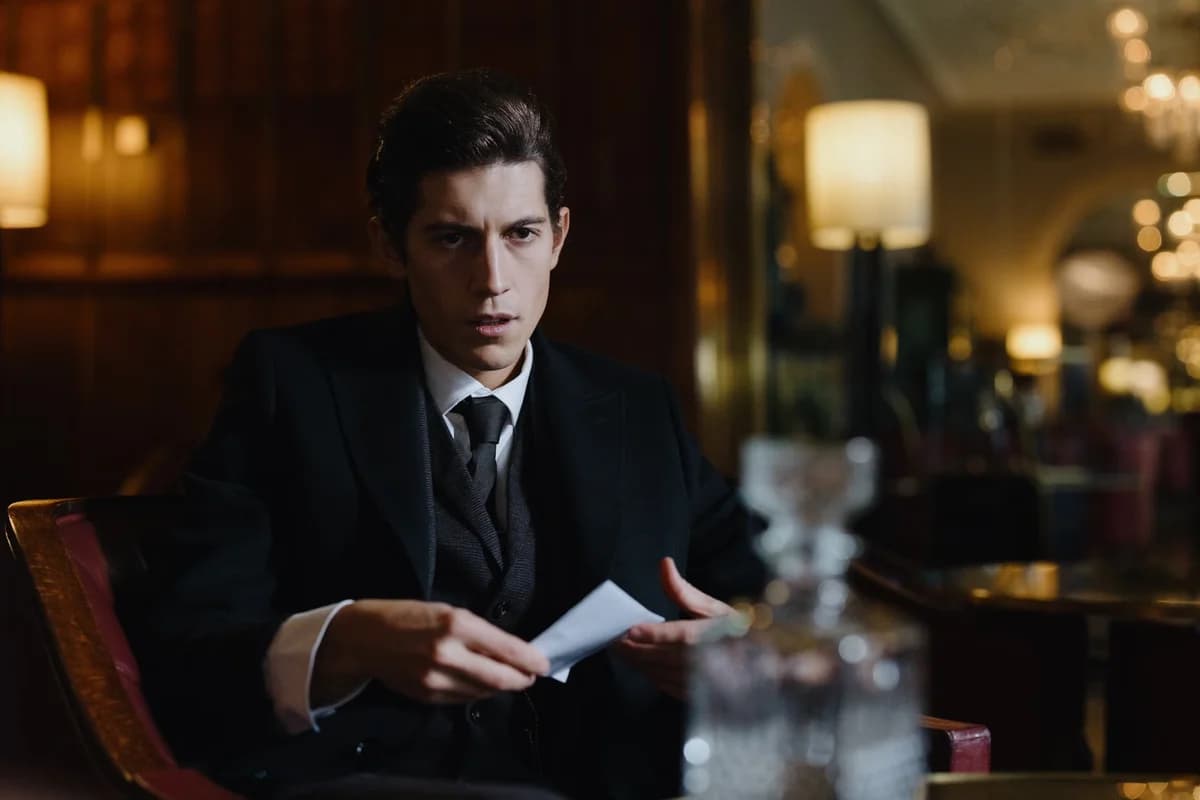 Man in a black suit holding a piece of paper in a dim lounge