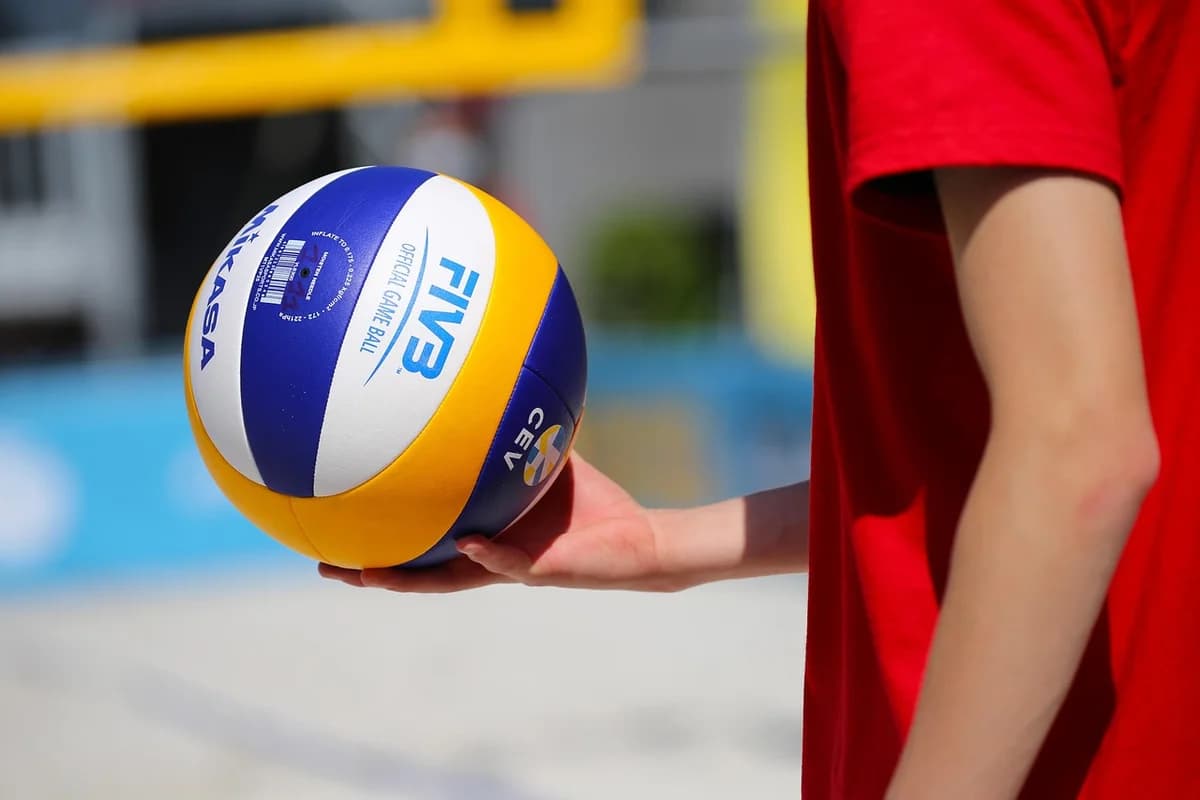 A person holding a beach volleyball on an outdoor court.