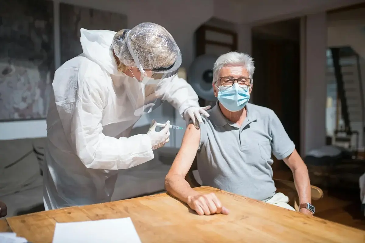 Healthcare worker giving COVID-19 vaccine to elderly man indoors