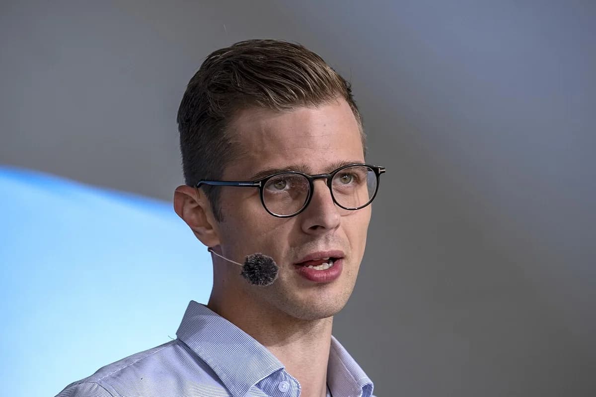 A man wearing glasses and a headset microphone speaks on stage.
