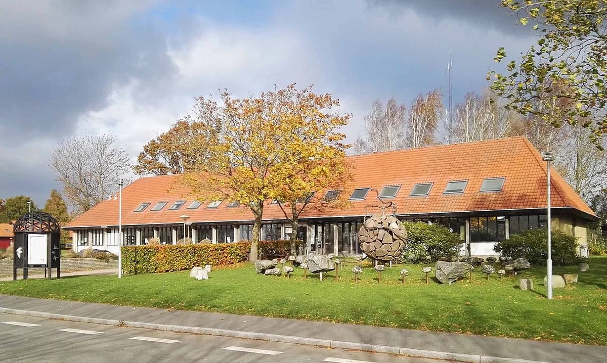 Long building with red roof and front lawn with stone sculptures