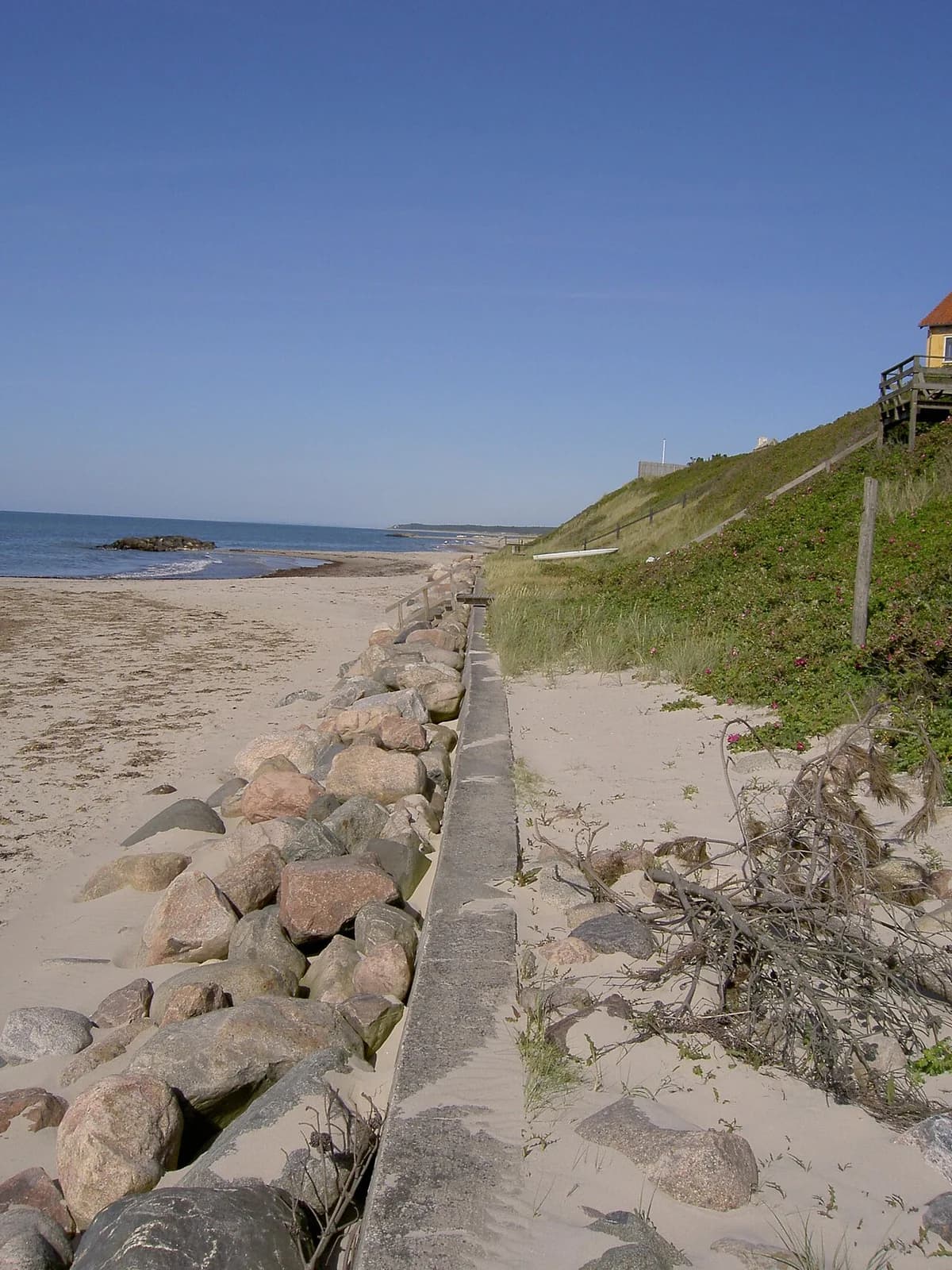 A wide sandy beach and calm sea beside a grassy dune.