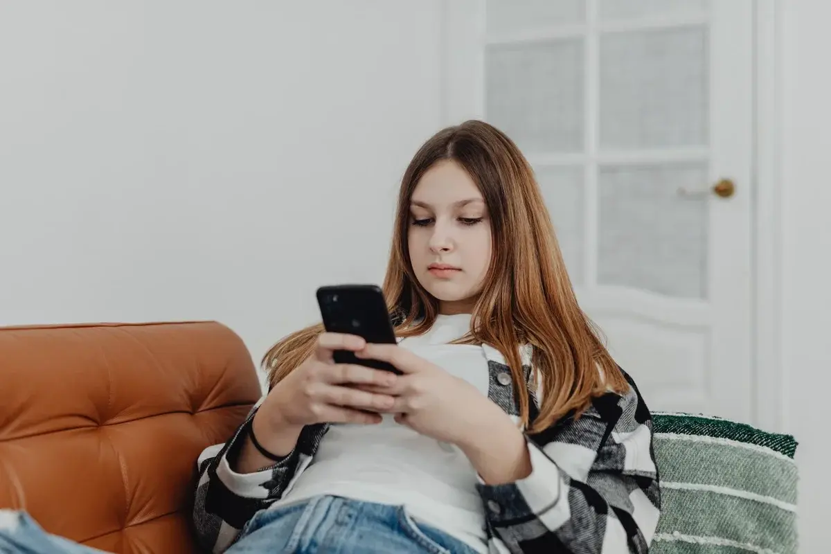 A teenage girl sitting on a sofa and using a smartphone indoors.