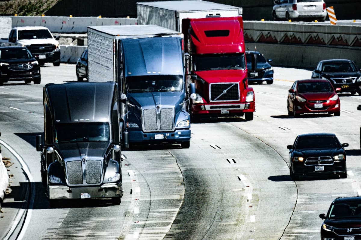 Several semi-trucks and cars traveling on a multi-lane highway in daylight.