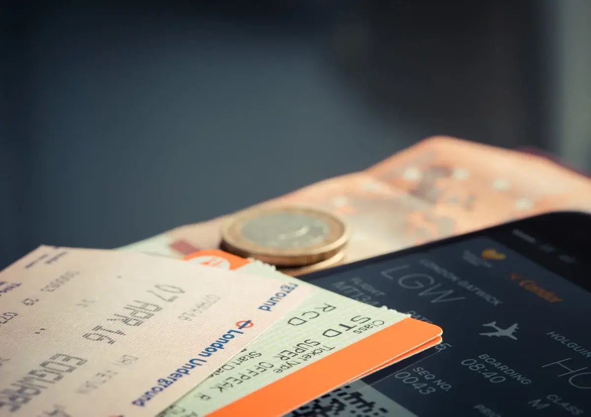 Close-up of a flight ticket, euro coins, and a smartphone showing flight details.