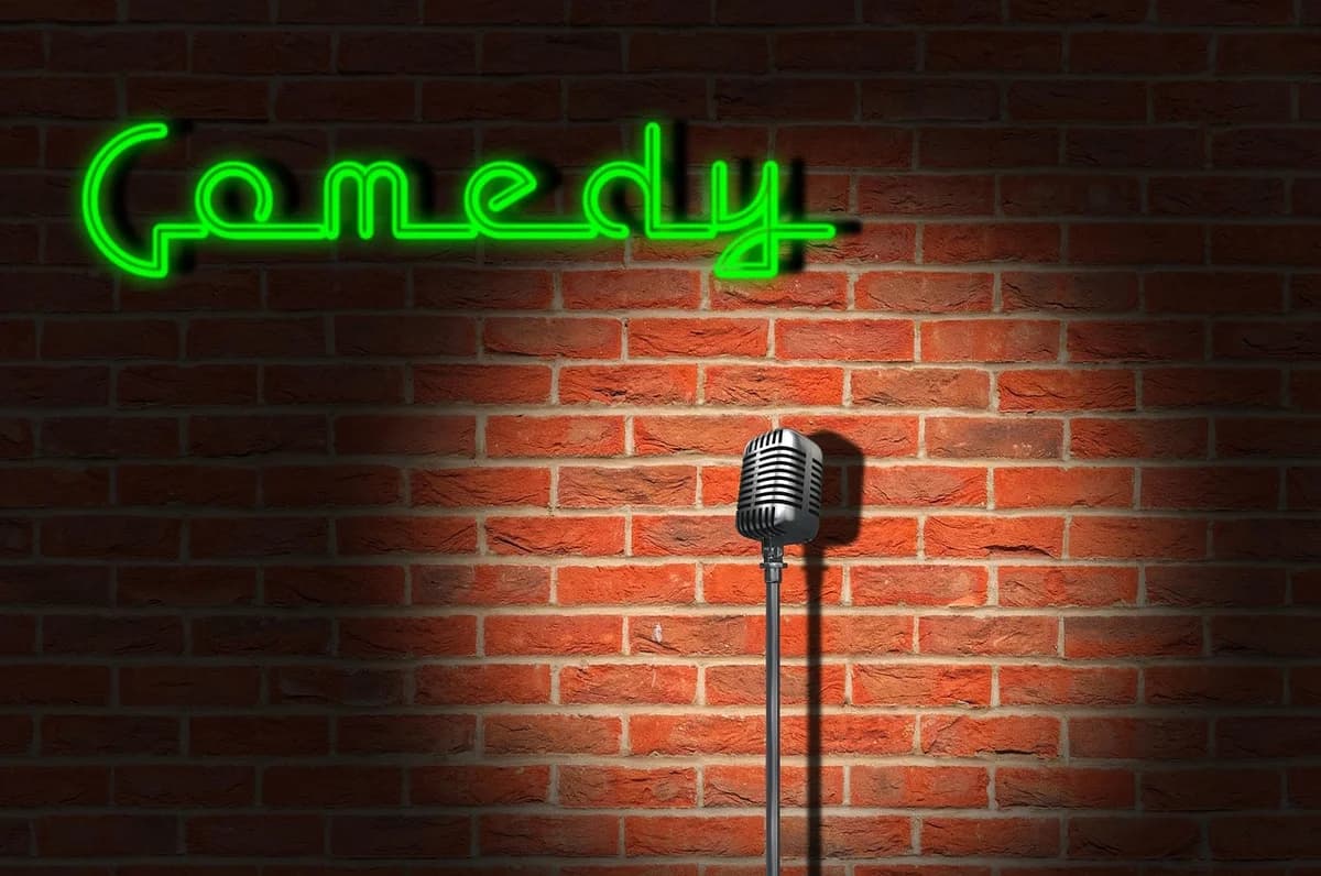 Microphone on a stand in front of a brick wall with a green neon comedy sign