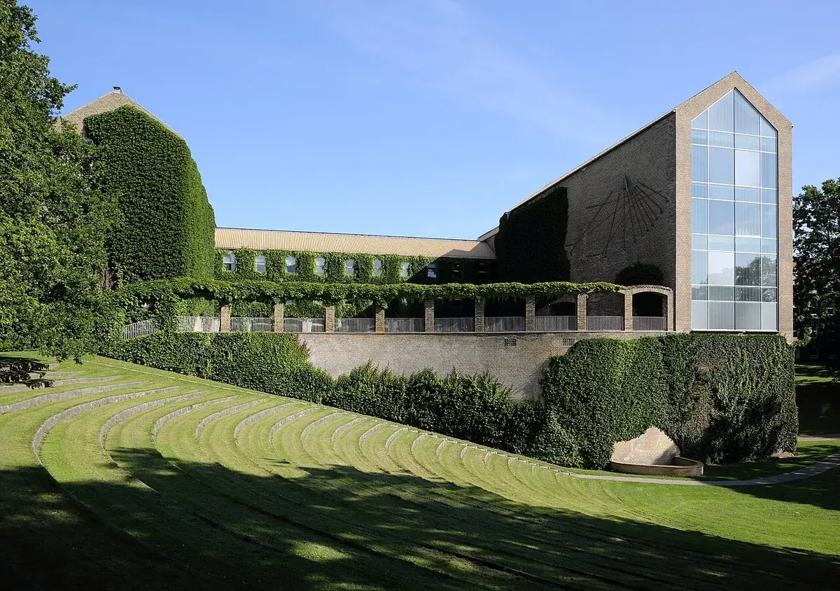 Aarhus University main building viewed from a park with green lawns and ivy-covered walls.