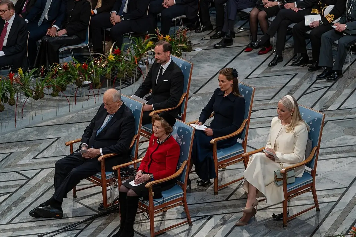 Formally dressed attendees seated at a ceremonial event in a large hall.