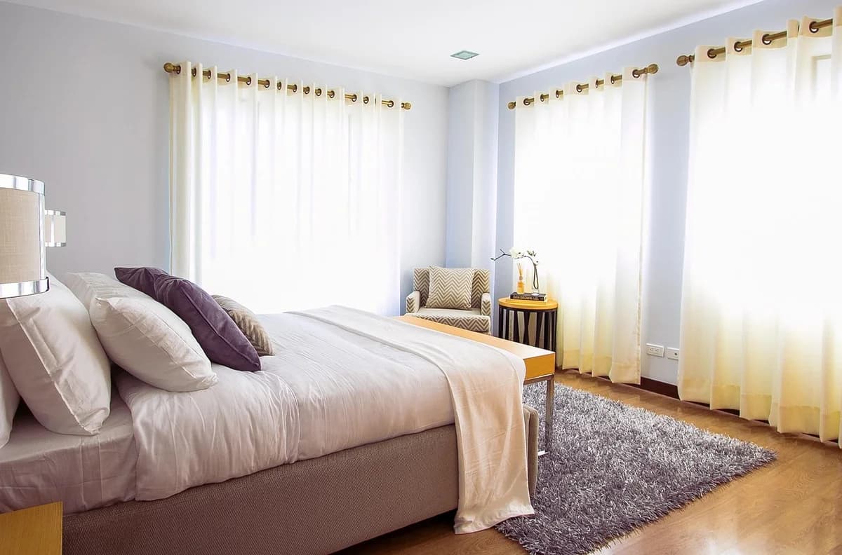 A bright bedroom with a bed, pillows, curtains, and a rug.